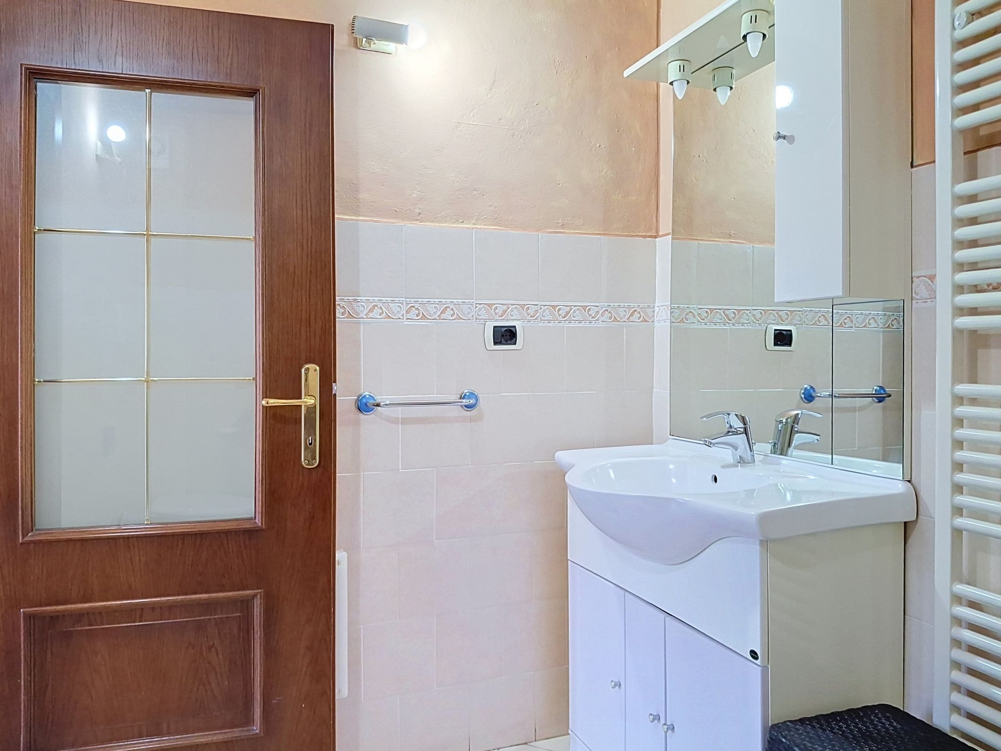 A bathroom with a wooden door, a white sink, a mirror, and a towel rack.