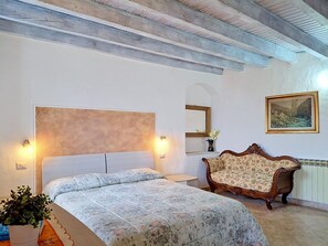 Ein Schlafzimmer mit einem Bett, einer hölzernen Bank, einem wandmontierten Spiegel und einem Gemälde.