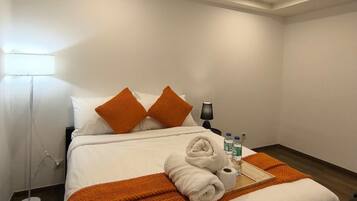 A hotel room with a bed, pillows, a lamp, a tray with toiletries, and a window.