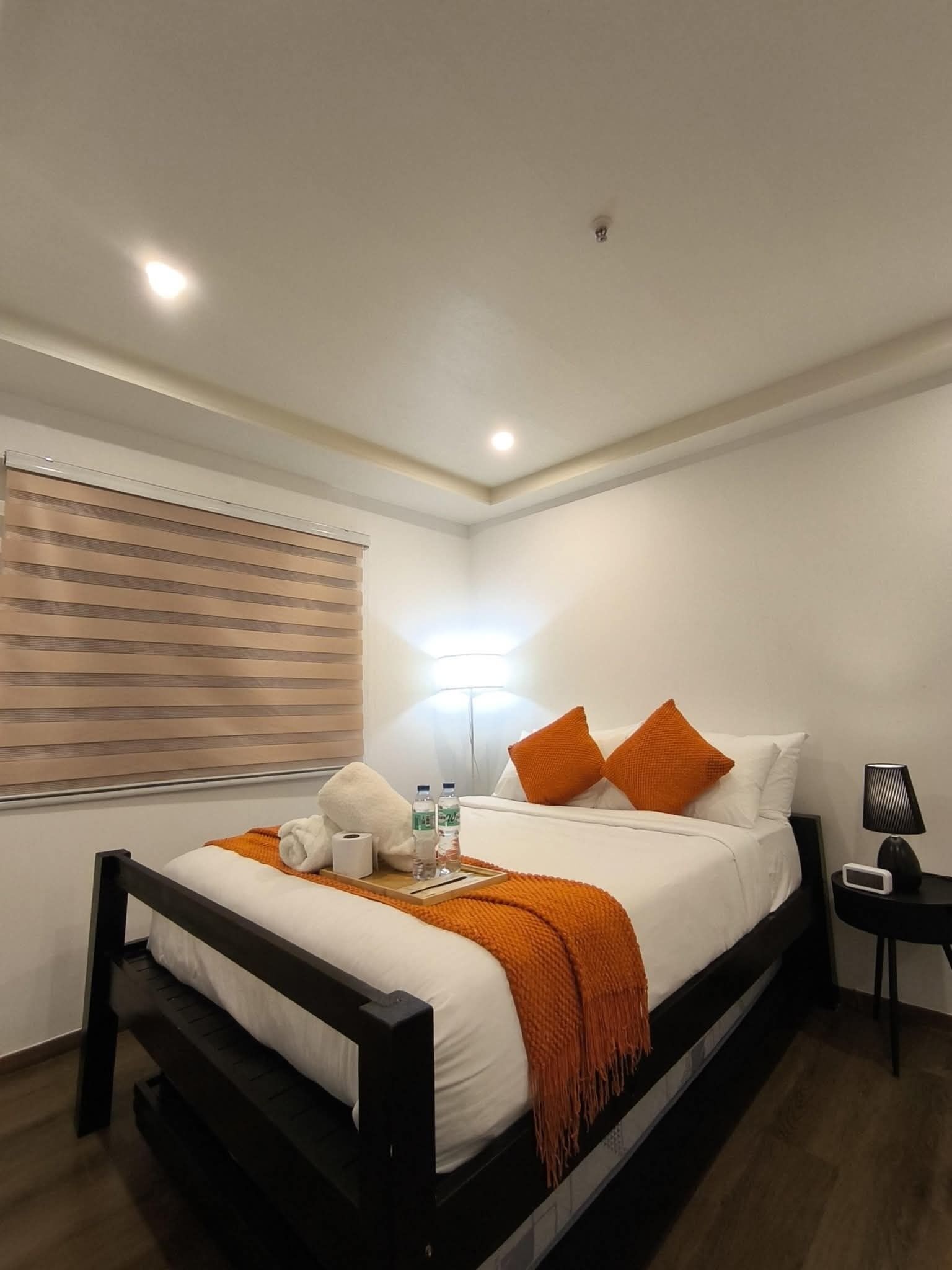 Ein Hotelzimmer mit Bett, Nachttisch, Lampe und einem Fenster mit Jalousien.