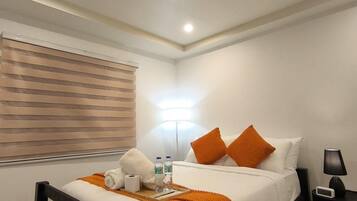 Ein Hotelzimmer mit Bett, Nachttisch, Lampe und einem Fenster mit Jalousien.