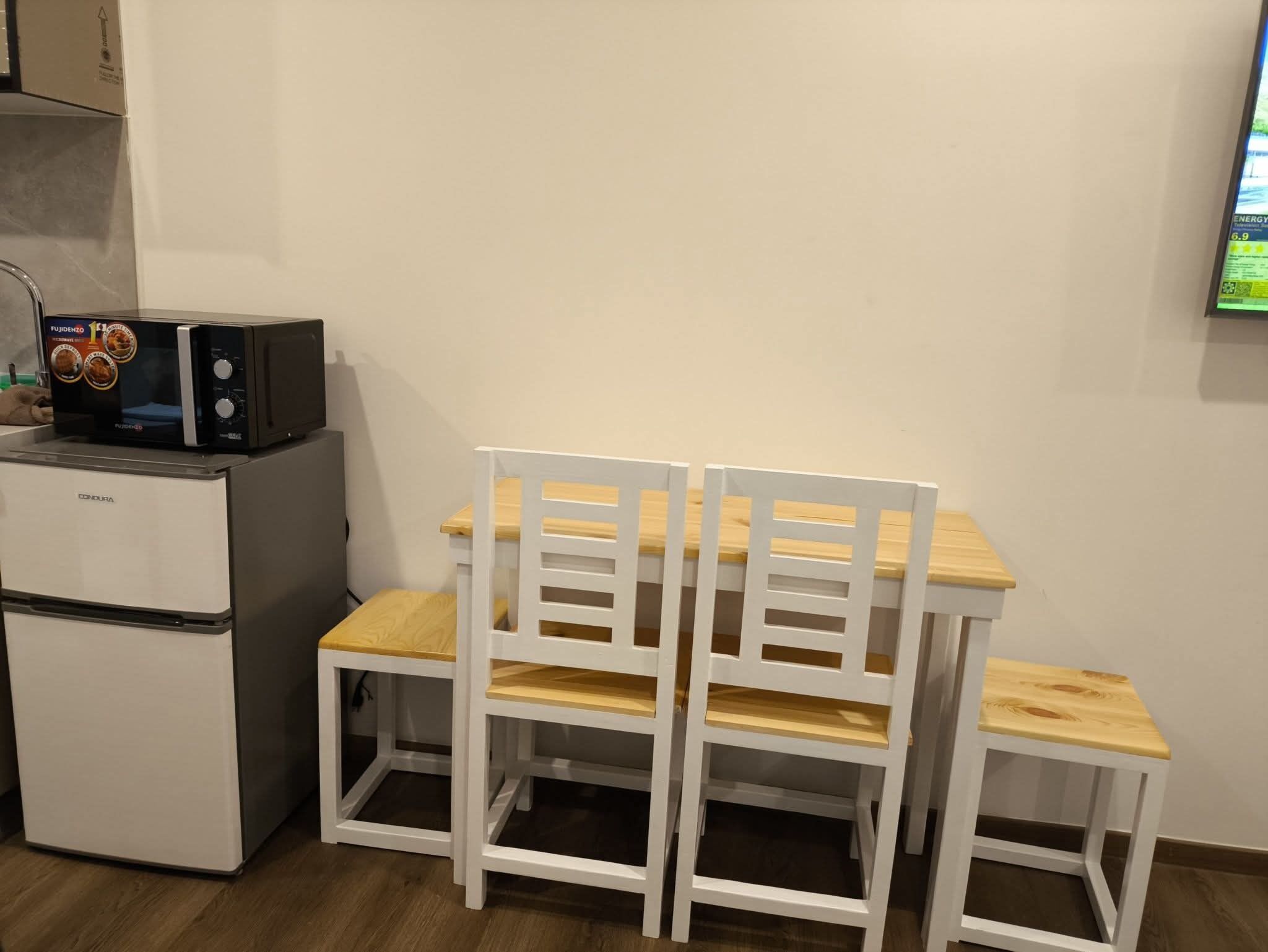 Eine Küchenzeile mit Kühlschrank, Mikrowelle und Holzkohle-Stühlen.