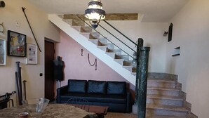 A staircase leading to an upper floor, a dining area with a table and chairs, a black sofa, and a chandelier. - Casal Trinacria - 1-Bedroom Apartment with Panoramic Jacuzzi (No. 5) (Sicilia)