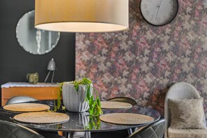 A dining table with placemats, a potted plant, and a hanging lamp. - Guestready - Rose and Monkey (Manchester)
