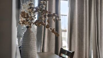 A dining table with a vase of dried flowers, a chair, and curtains.