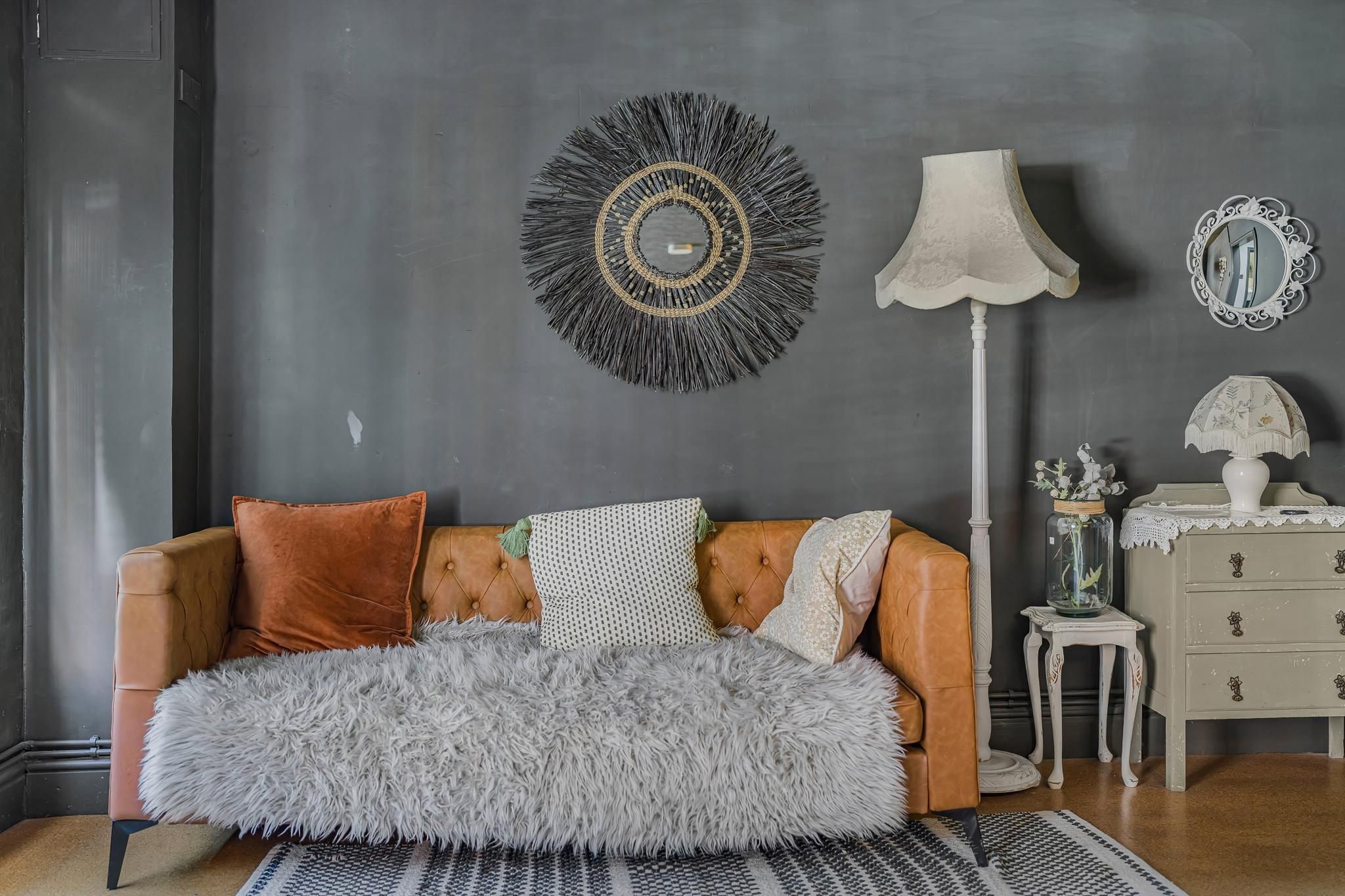 A room with a sofa, a lamp, a mirror, a vase, and a small table.