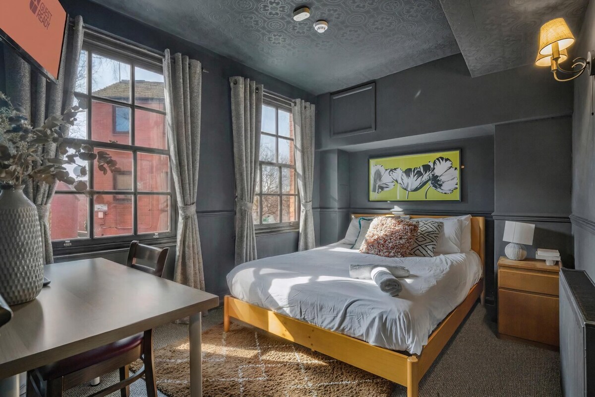 A bedroom with a bed, bedside table, lamp, and a painting on the wall.