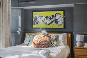 A neatly made bed with white linens, a fluffy orange and white pillow, and a framed black and white floral artwork on the wall above. - Guestready - Rose and Monkey (Manchester)