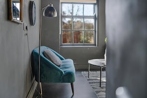 A room with a teal sofa, a round table, a floor lamp, and a window with a view of trees. - Guestready - Rose and Monkey (Manchester)
