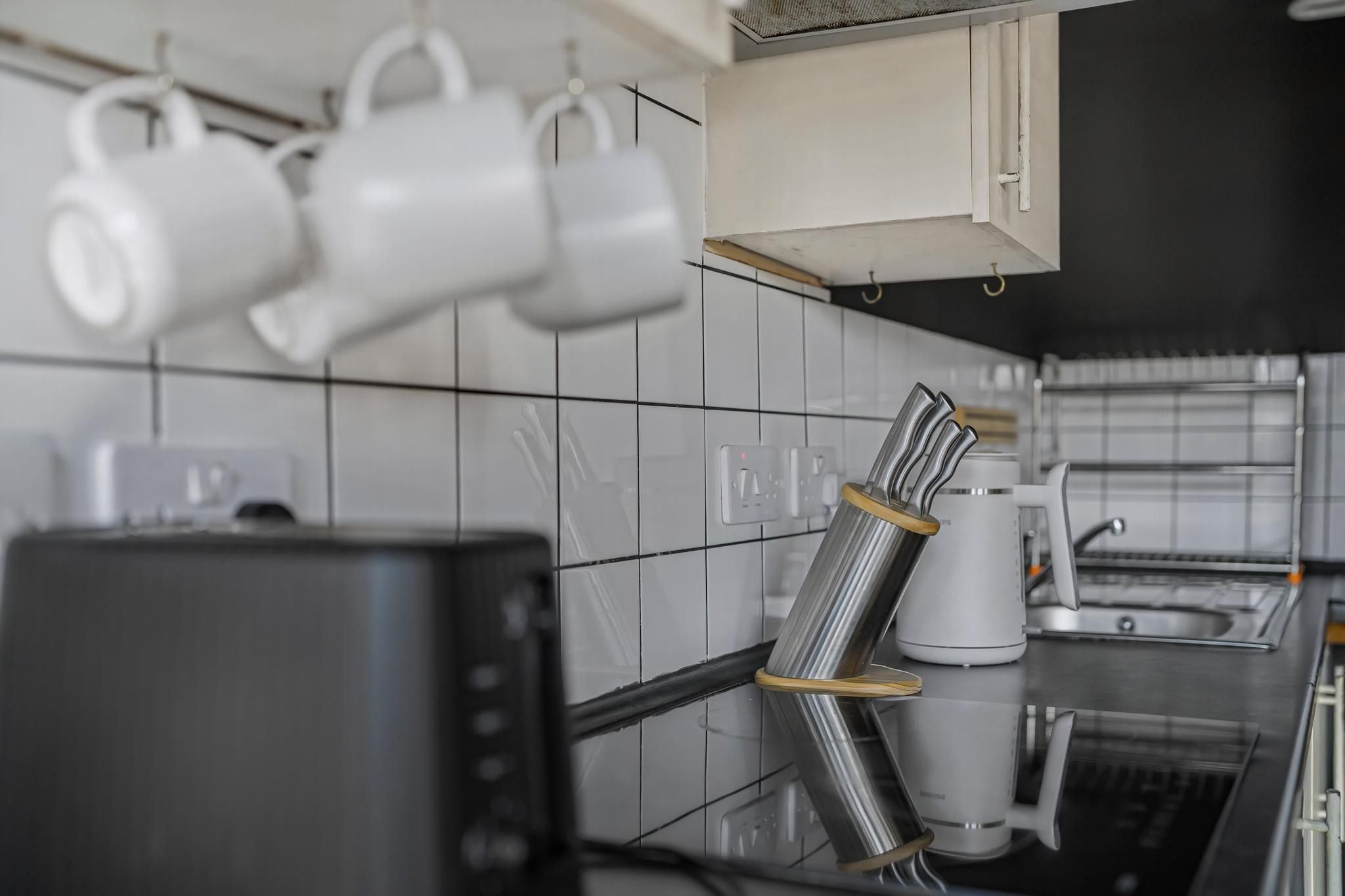 A kitchen with white tiles, a coffee maker, and a kettle.