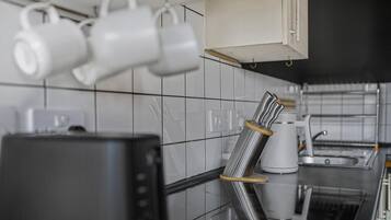 A kitchen with white tiles, a coffee maker, and a kettle.