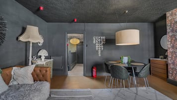 A modern living room with a sofa, a dining table with chairs, a fireplace, and a ceiling with patterned design.