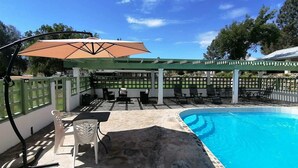Un espace piscine agrémenté d’une pergola, de coins salon extérieurs et d’une terrasse couverte.