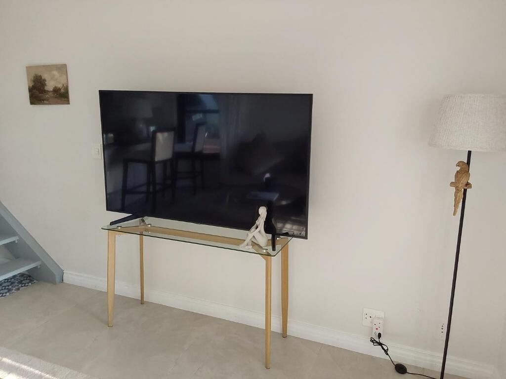 A flat-screen TV on a glass table with a statue, a lamp, and a staircase in the background.