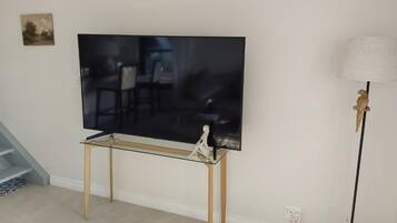 A flat-screen TV on a glass table with a statue, a lamp, and a staircase in the background.