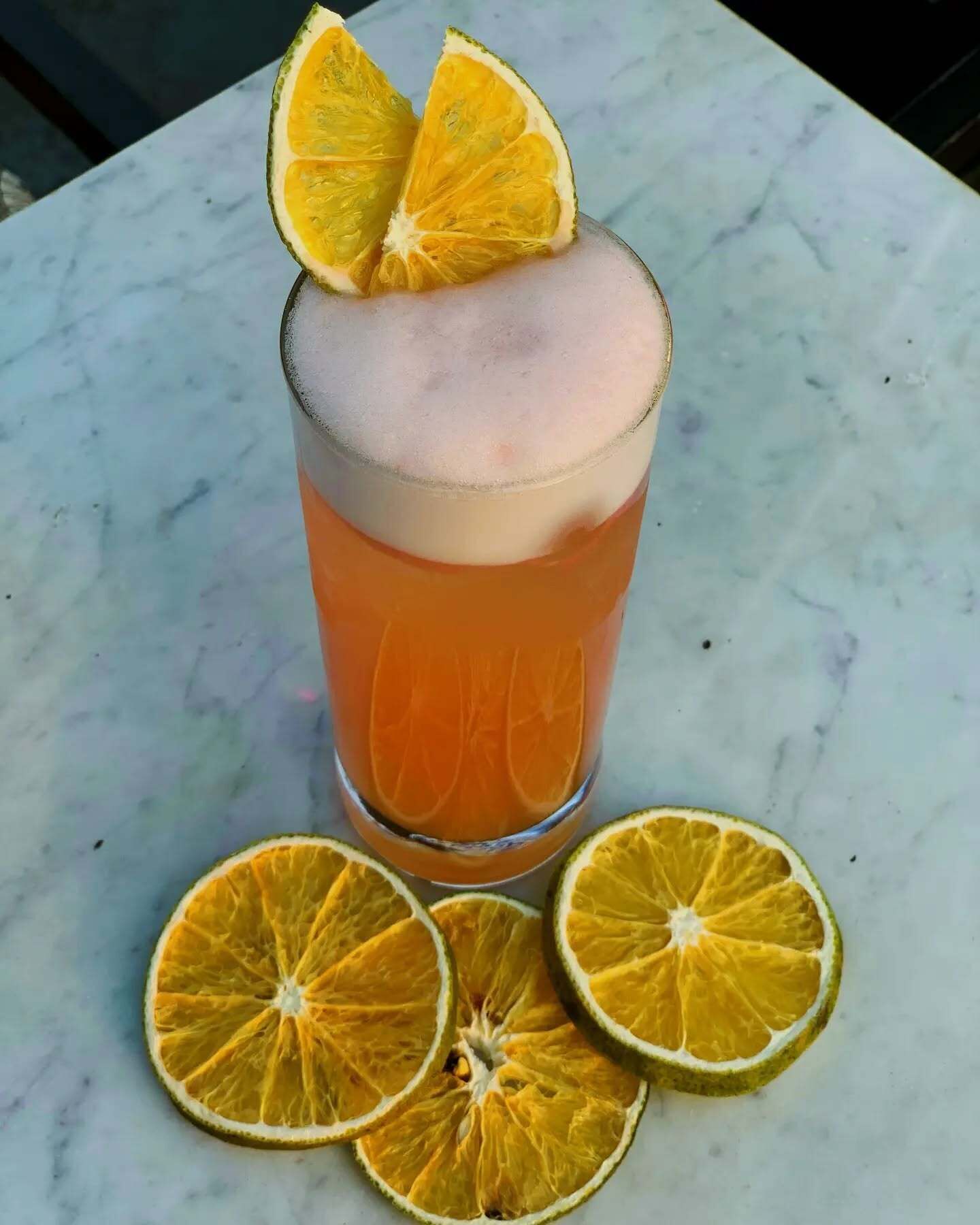 Un vaso de bebida anaranjada con hielo, adornado con rodajas de naranja, sobre una superficie de mármol.