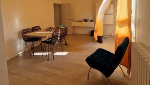Un grand espace de vie comprenant une table à manger, des chaises, un fauteuil bleu, un escalier et un radiateur.