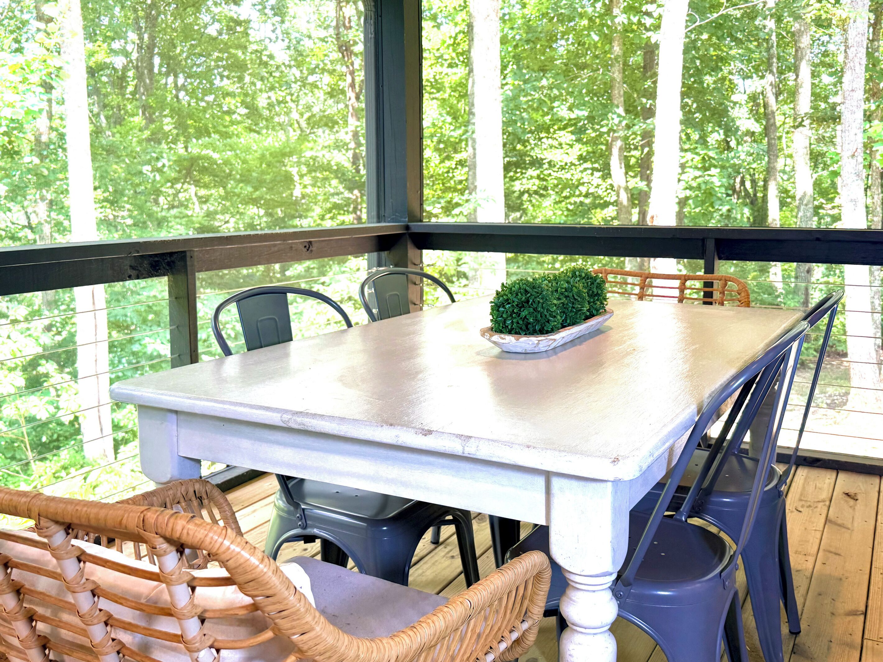 A table with chairs on a wooden deck, overlooking a forest.