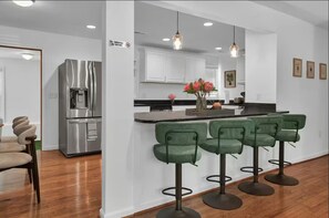 Una cocina moderna con un refrigerador de acero inoxidable, una zona de bar con taburetes verdes y una isla central con un jarrón de flores.