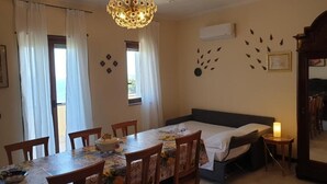 Een kamer met een bed, een eettafel met stoelen, een kroonluchter en een tafeltje met een kaars.