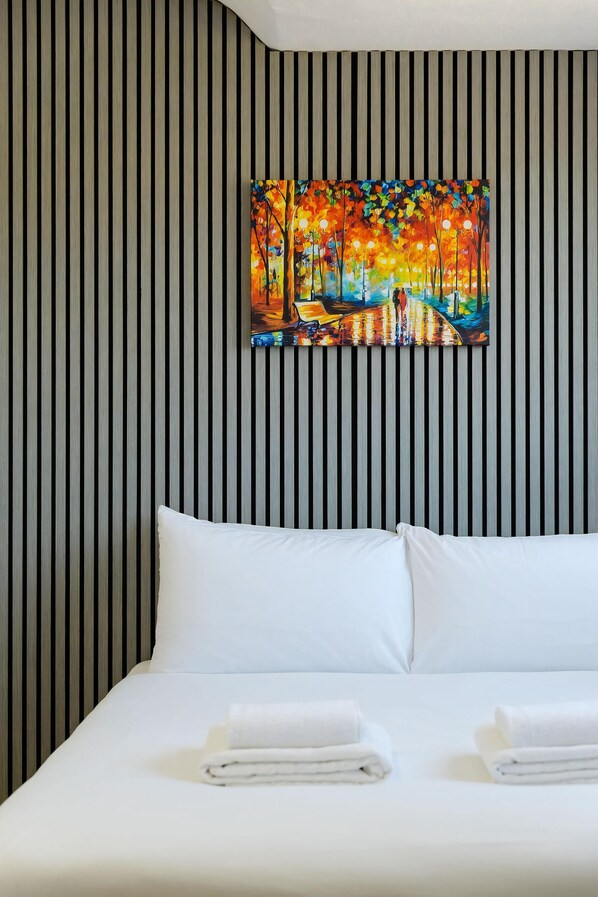A hotel room with a striped wall, a bed with white linens, and a painting of a colorful landscape. - Southern Cross (Watford)