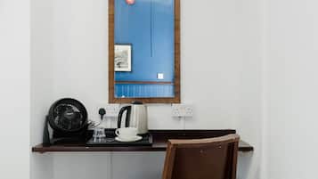 Un pequeño escritorio con una tetera, una taza y un ventilador.