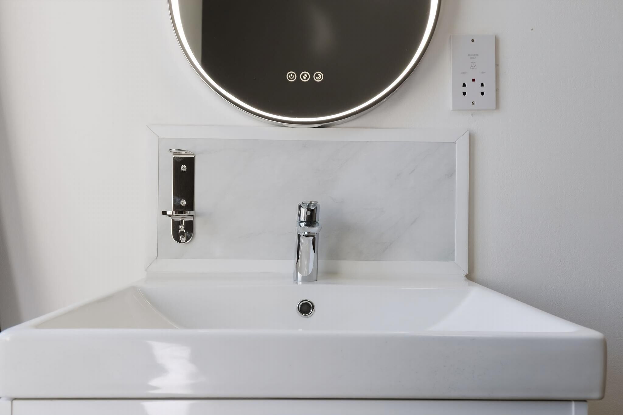 A bathroom with a white sink, a mirror, and a wall-mounted light.