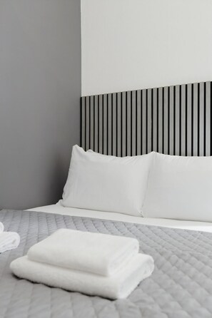 A neatly made bed with white bedding, a grey quilted duvet, and a black and white striped headboard. - Southern Cross (Watford)