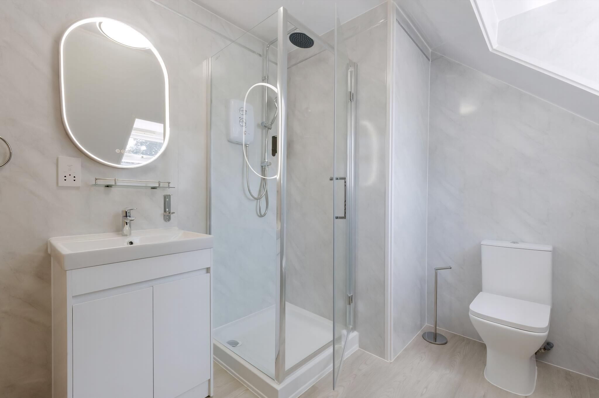 Un baño moderno con ducha envuelta en vidrio, un lavabo blanco con espejo y un inodoro.
