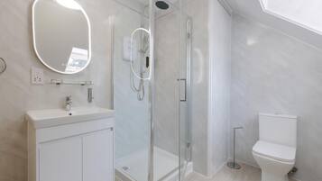 Un baño moderno con ducha envuelta en vidrio, un lavabo blanco con espejo y un inodoro.