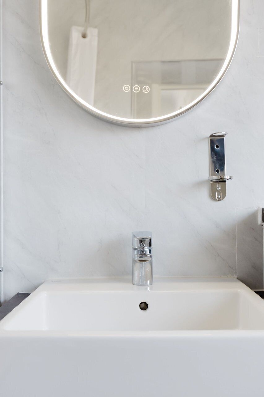 Un baño con un lavamanos blanco, un espejo redondo y un toallero.