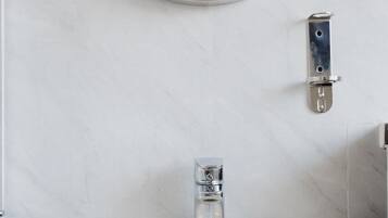 Un baño con un lavamanos blanco, un espejo redondo y un toallero.