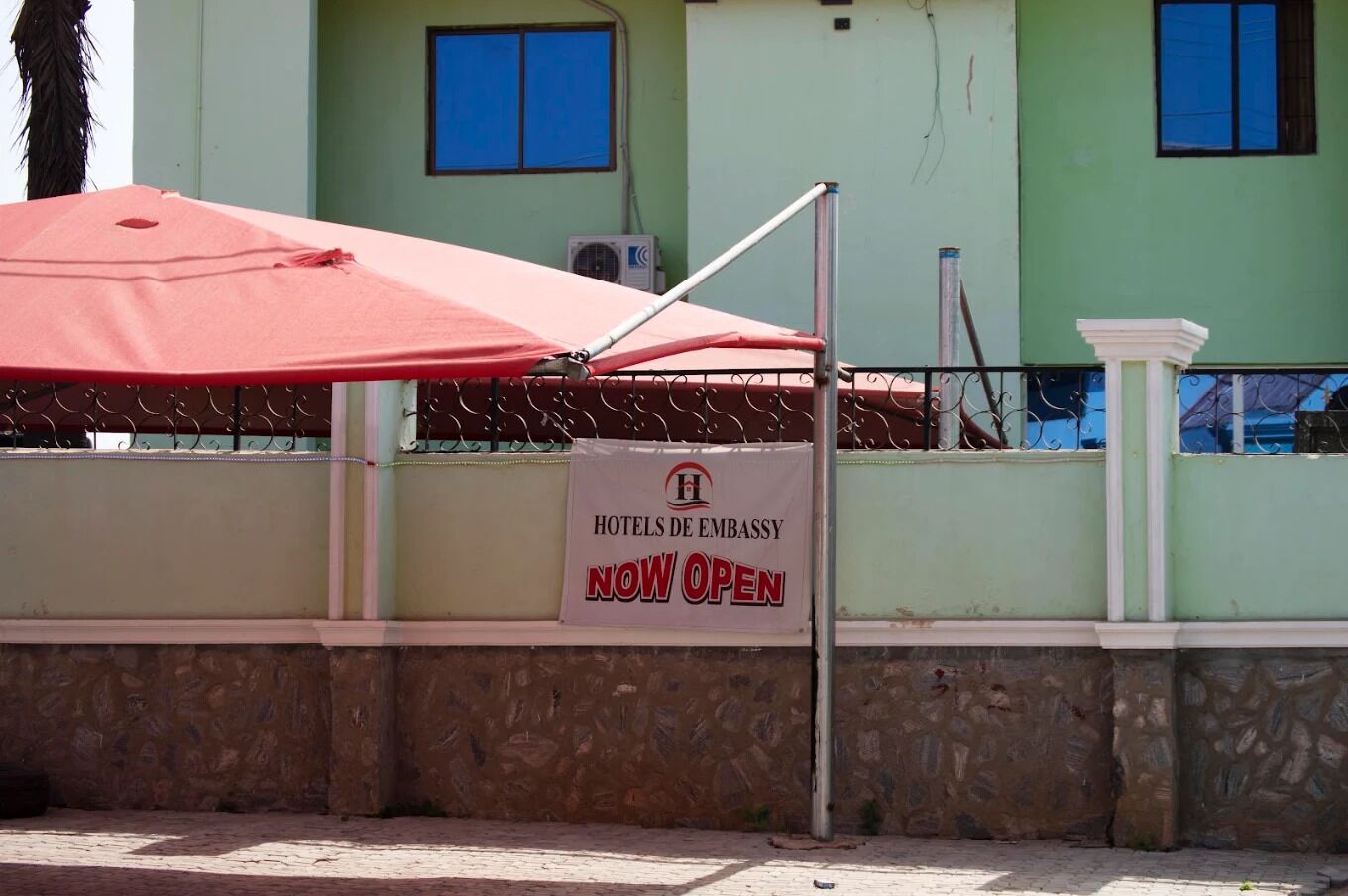 A sign indicating the hotel is now open, with a red umbrella and metal fence in the foreground.