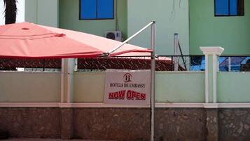 A sign indicating the hotel is now open, with a red umbrella and metal fence in the foreground.