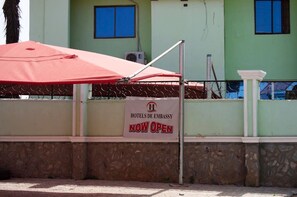 Señal que indica que el hotel está ahora abierto, con un paraguas rojo y una valla metálica en primer plano.