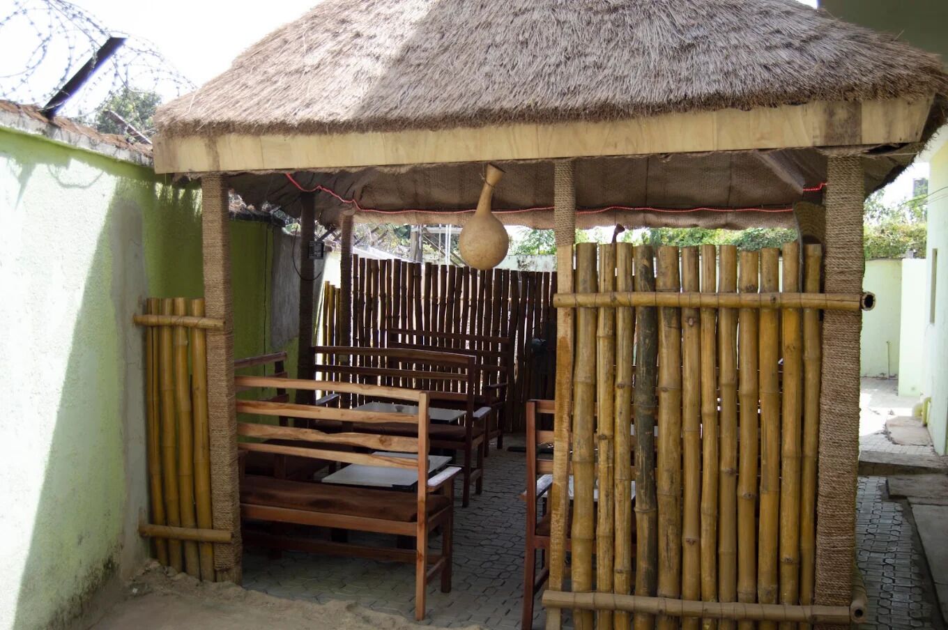 Una estructura con techo de paja, bancos de madera y cerca de bambú.