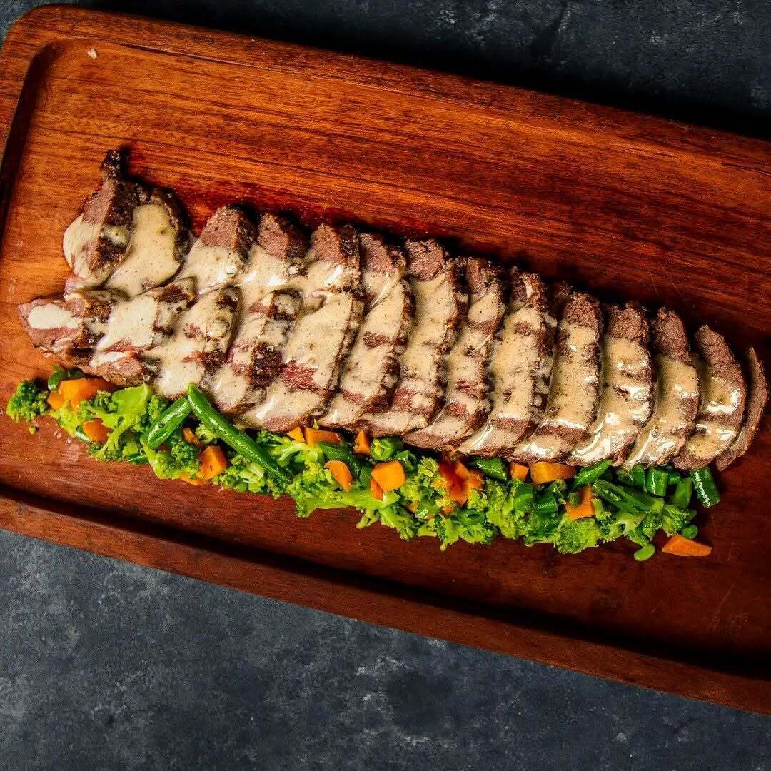 Una tabla de madera con carne cortada y una ensalada de verduras.