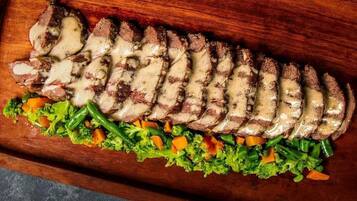 Una tabla de madera con carne cortada y una ensalada de verduras.