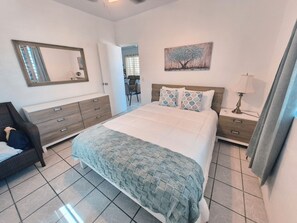 A bedroom with a bed, a dresser, a nightstand, a lamp, a painting, and a mirror. - 3-bedroom cottage in Vieques w Wifi,  AC, breeze, free parking and pets friendly (Vieques)