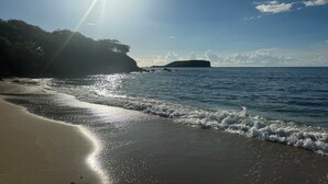 A beach with sunlight reflecting off the water, a sandy shore, and a distant island.