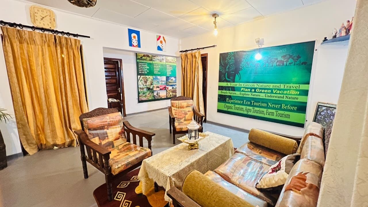 A living room with a sofa, chairs, a table, and curtains. There are posters on the walls and a clock on the wall.