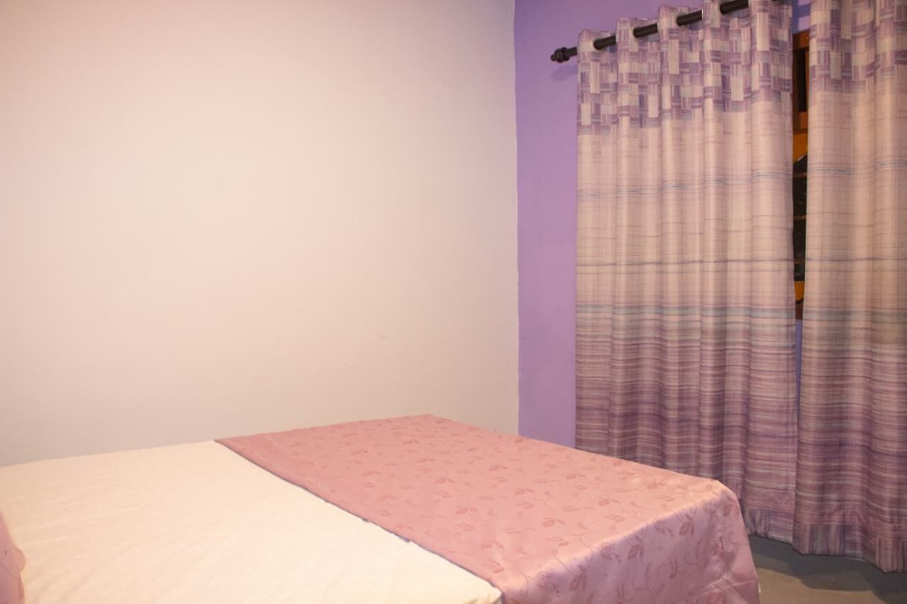 Una habitación con una cama individual, una pared morada y una cortina.