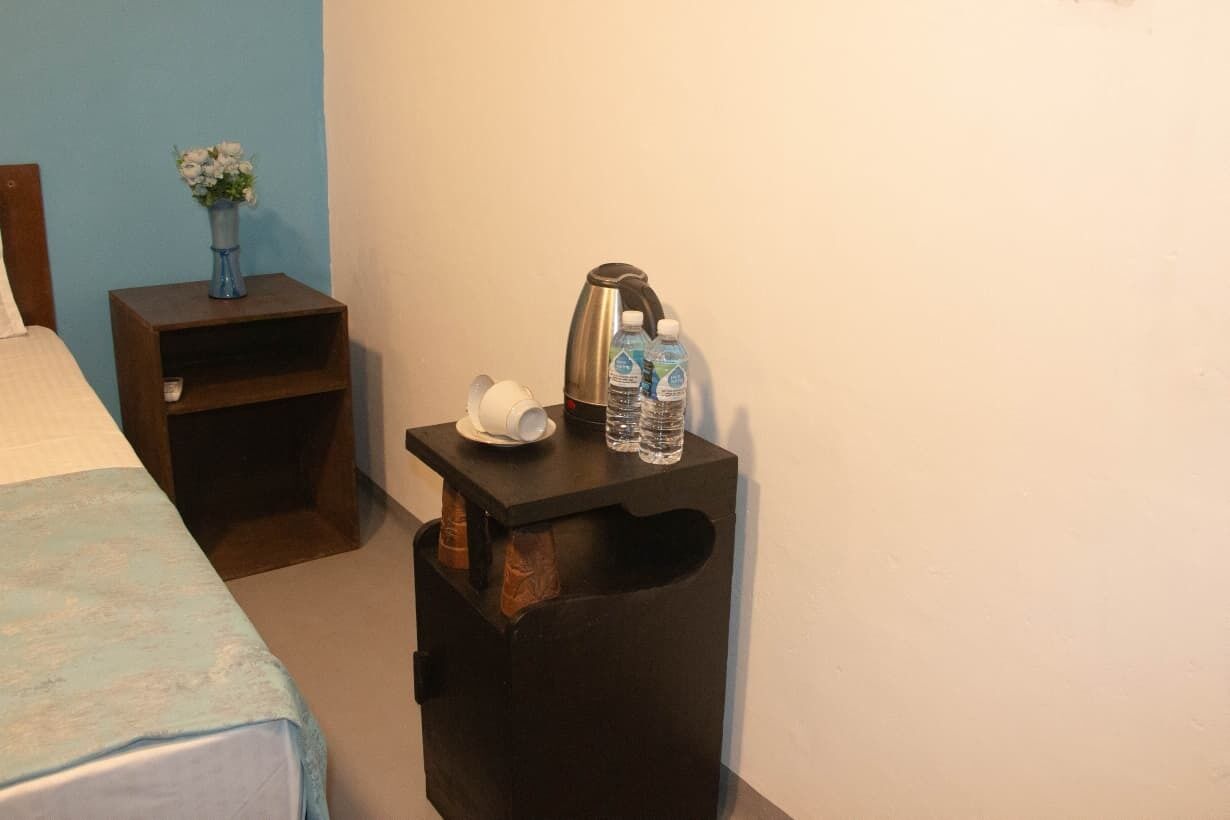 Une chambre d’hôtel avec un lit, une table de chevet ornée d’un vase de fleurs, une machine à café et deux bouteilles d’eau.