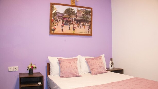 Un dormitorio con cama, dos mesitas de noche, un cuadro en la pared y una pequeña mesa con un florero.