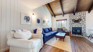 Een woonkamer met een bank, fauteuil, open haard en kunstwerken in lijsten.