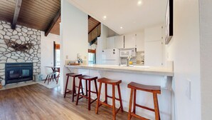 Een moderne keuken met een stenen openhaard, houten barstoelen en witte kasten.