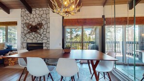 Een eetgedeelte met een grote houten tafel, witte stoelen, een stenen muur en een kroonluchter.