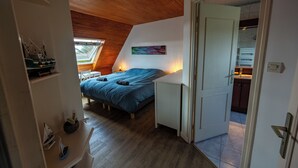 Ein Schlafzimmer mit schrägen Wänden, einem Bett mit blauer Bettwäsche, einem kleinen Tisch und einem an der Wand befestigten Regal mit Dekorationen.