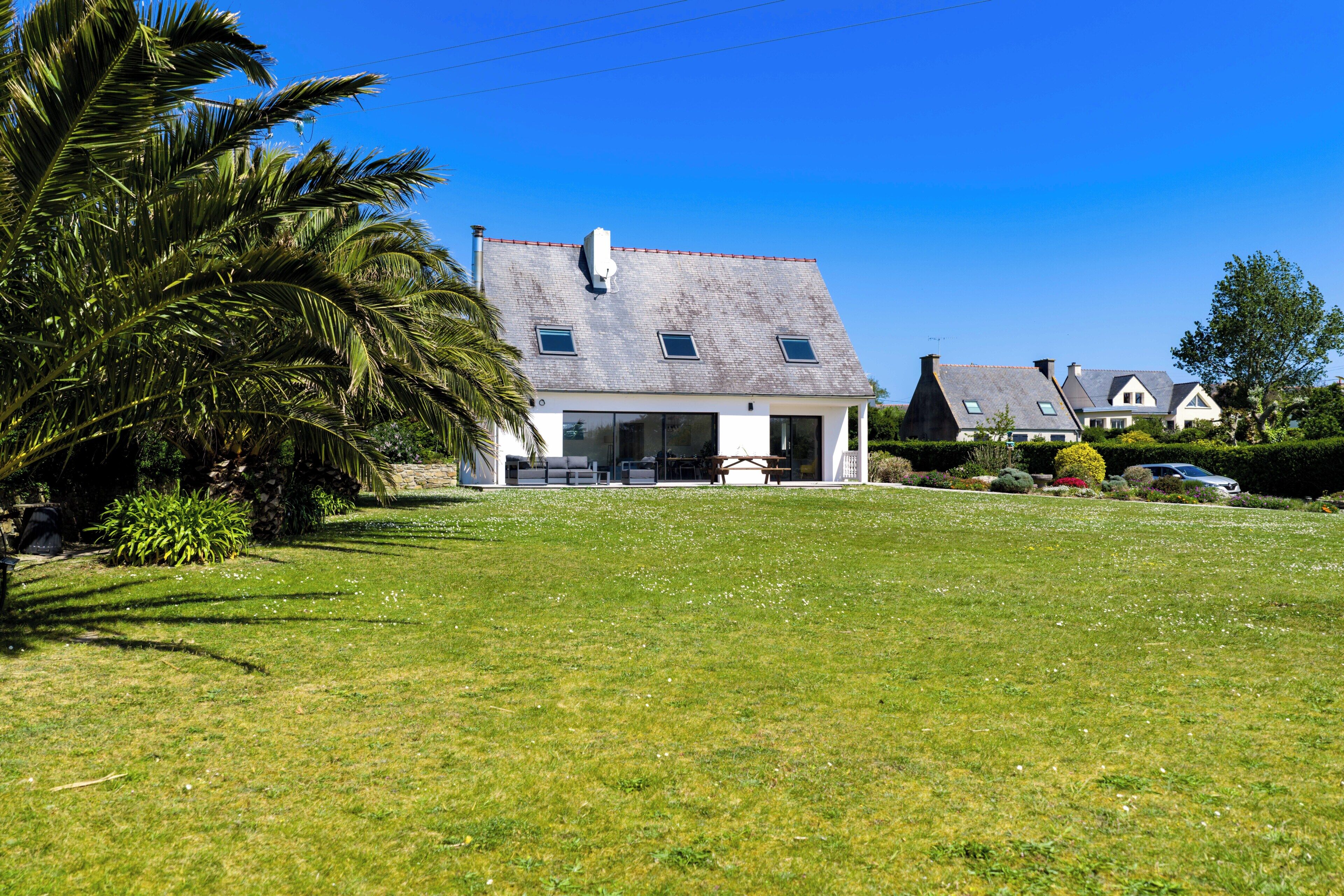A house with a sloped roof, a large lawn, and a palm tree.