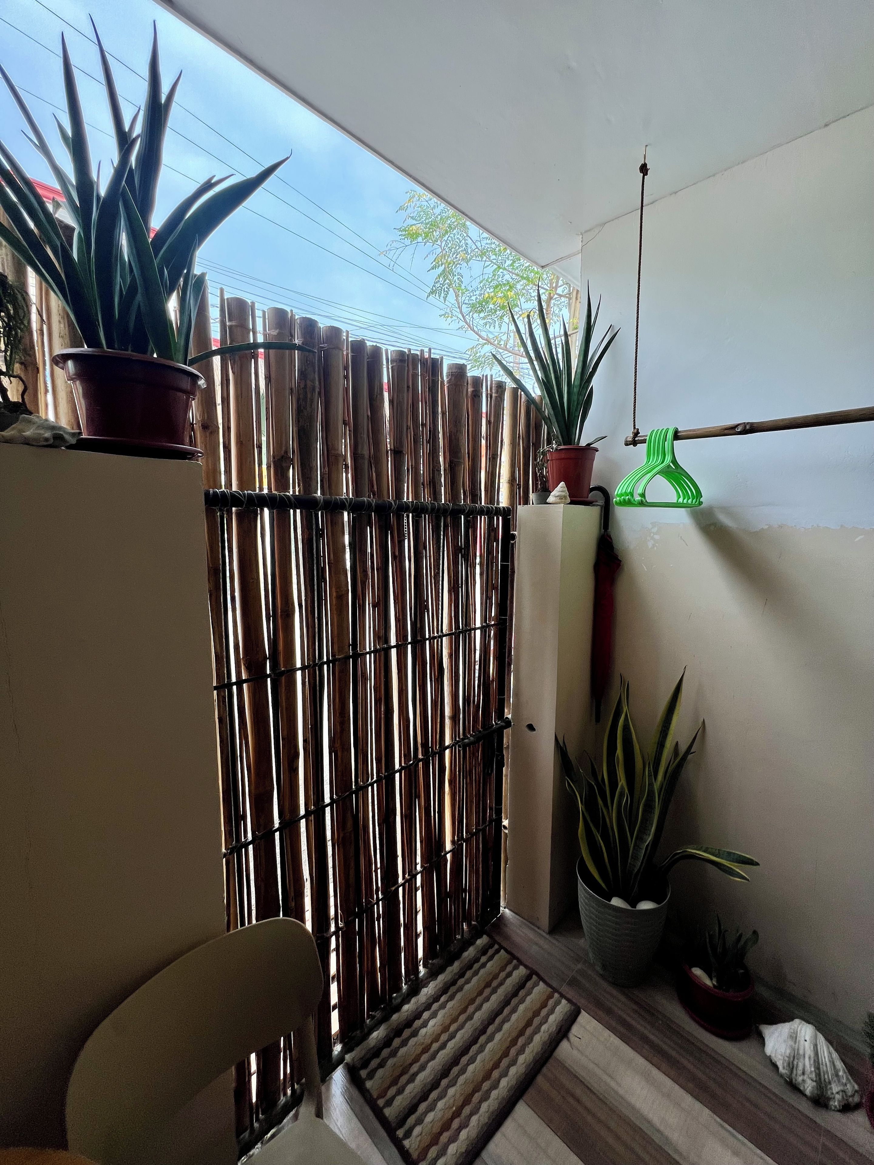 A balcony with a bamboo fence, potted plants, a chair, and a doormat.